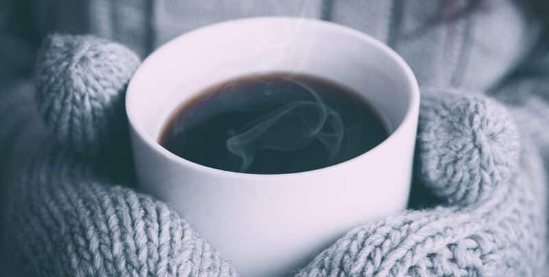 closeup of a cup of coffee being held by hands that are wearing gloves