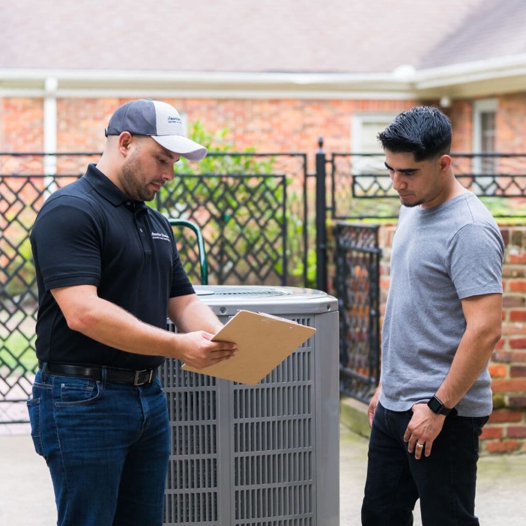 american standard technician talking to homeowner while showing him something on a clipboard while standing next to outdoor hvac unit that is about to be installed