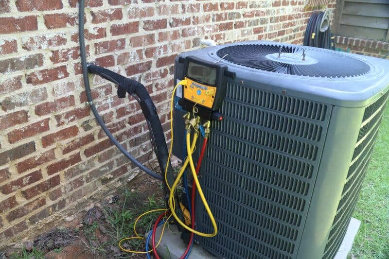 hvac unit positioned outside of a home with a pressure reader on it having maintenance performed on it