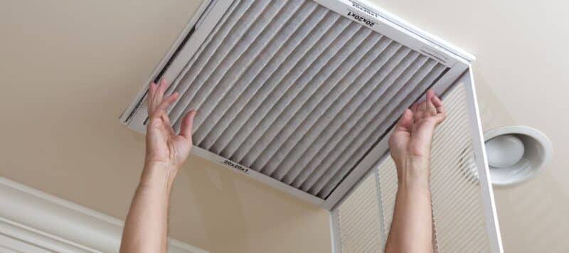 Person installing or replacing an air filter in a ceiling vent